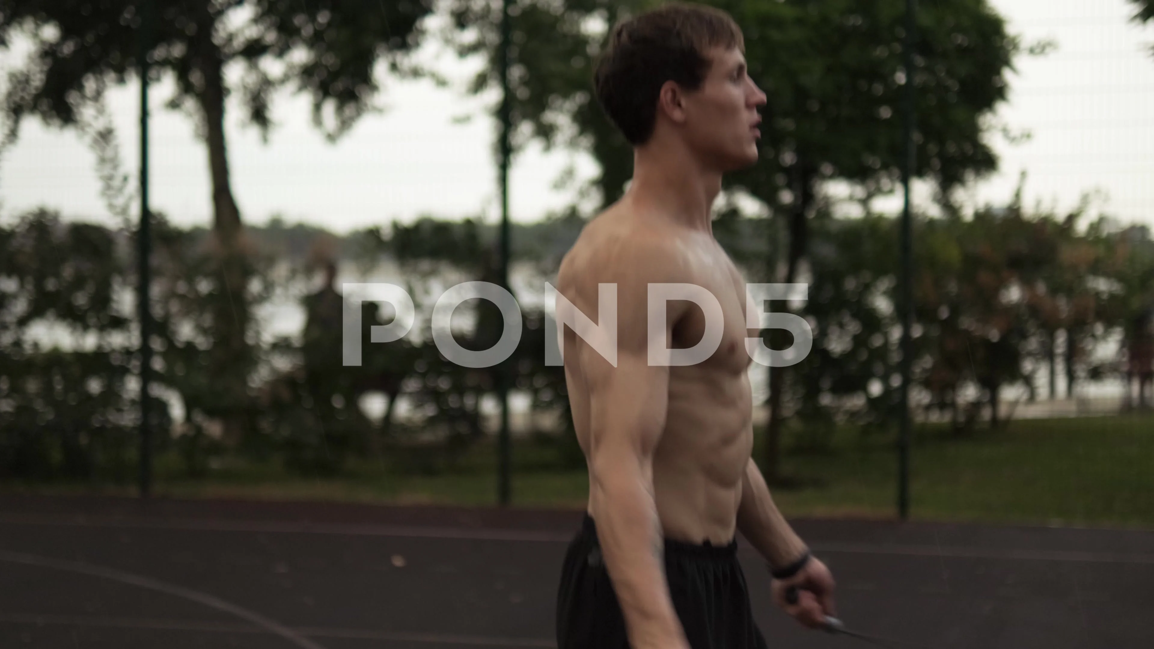 A half naked guy is jumping with a rope while training outside