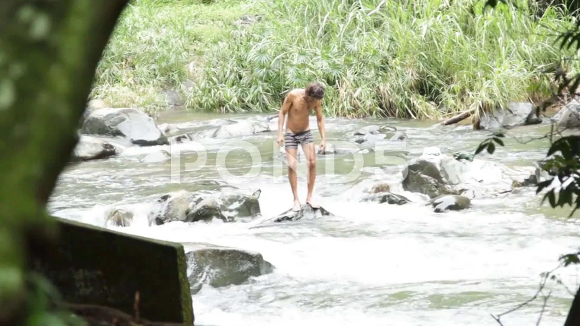 Half-naked homeless man making strange gestures on the rock of a river