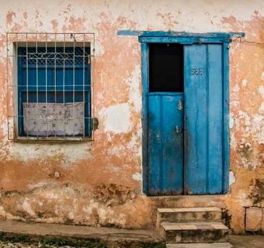 Half-open blue door plus window with grate on tattered yellow wall with stone Stock Photos