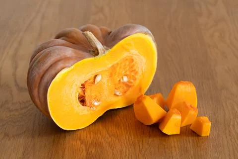 Half of an orange pumpkin next to diced pumpkin pulp on a wooden kitchen tabl Stock Photos