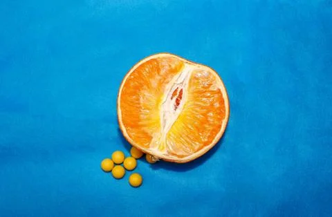 Half an orange with round vitamins of ascorbic acid lying next to it. Stock Photos