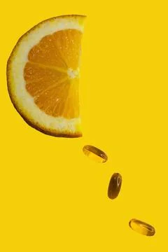 Half orange slice and vitamins falling as drops on yellow background. Stock Photos