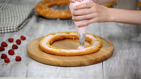 Half of a Paris Brest cake. Background: a pastry bag filling with whipped cream. Stock Footage 93927237