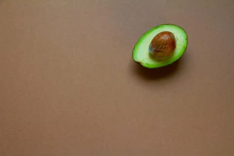 Half of raw avocado on brown background, creative food concept Stock Photos