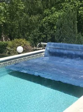 Half removed blue solar pool cover with clean swimming pool water surrounded by  Stock Photos