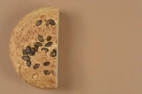 Half of Round Bread Loaf with Pumpkin Seeds on Brown Background Stock Photos