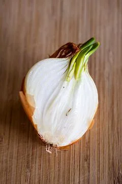 A half of a sprouting bulb or common onion and lying on a wooden cutting boar Stock Photos