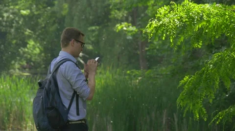 Half Turned Man Clicks a Smartphone in Summer Park Holding a Mobile Phone Stock Footage 63811126