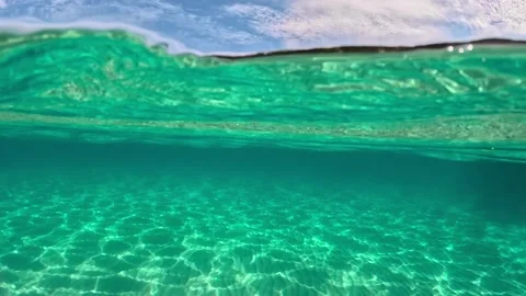 Half underwater slow-motion view of sandy beach bottom and rock with trees Video stock 219956515