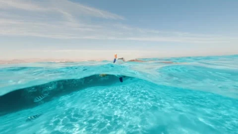 Half underwater split shot of snorkeler floating in calm transparent blue water Video stock 336592563