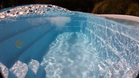 Half-underwater view of a tranquil blue pool with curved steps and water jets Stock Photos