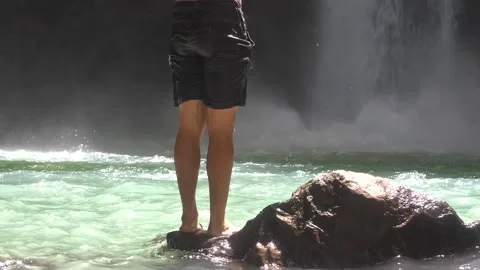 Half view of a man standing on a rock near and in front of a waterfall. Stock Footage 194351254