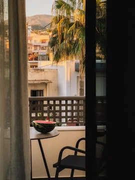 Half watermelon with spoon on small table on balcony overlooking city with palm Foto stock