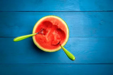 Half watermelon with spoons in it on a blue table Stock Photos