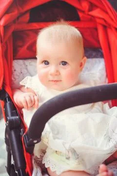 Half-year-old child in a stroller, a little girl in a white dress in a red st Stock Photos