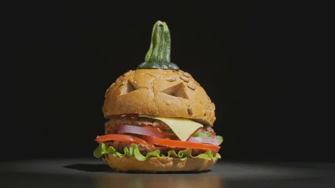 Halloween beef burger in shape of pumpkin rotating on black background Video stock 137744255