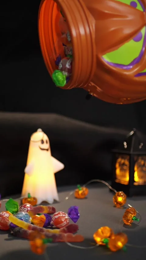 Halloween candy spilling from pumpkin bucket by a glowing ghost light Stock Footage 342521784