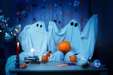 Halloween couple in ghost sheets holding pumpkin for party at home. Festive.. Stock Photos