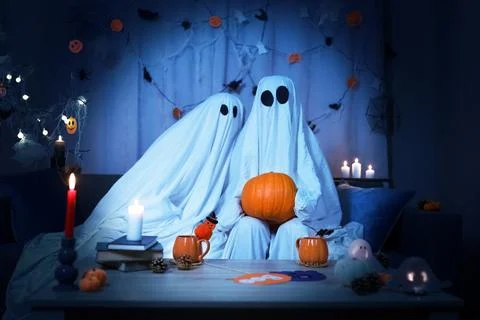 Halloween couple in ghost sheets holding a pumpkin for a celebration. Festi.. Stock Photos