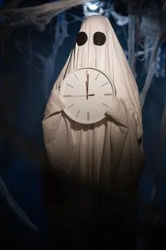 Halloween ghost in white sheet with black eyes holding alarm clock 12 oclock Stockfoto's