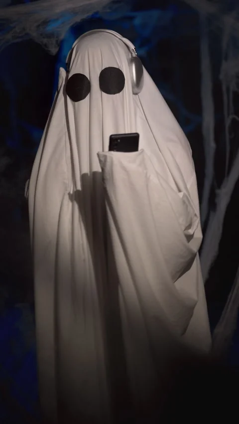 Halloween ghost in white sheet in dark corridor with spider web listening music Stock Footage 313735708