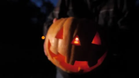 Halloween pumpkin appears from the darkness in the hands of a woman close-up Stock Footage 253311642