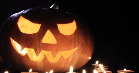 Halloween pumpkin head jack lantern with burning candles over black background Stock Footage