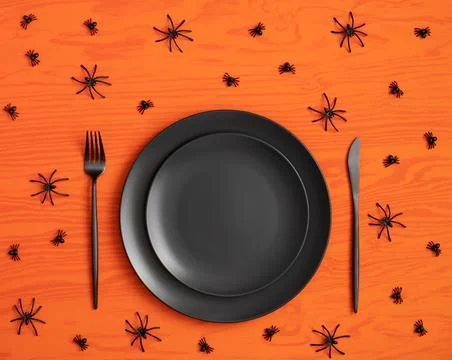 Halloween table setting. Empty black plate and cutlery, spiders on orange bac Stockfoto's