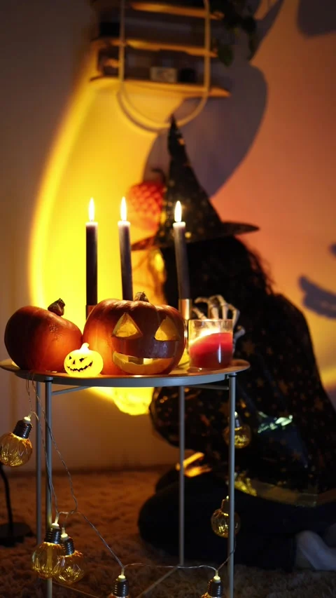 Halloween witch hides behind glowing pumpkins and burning candles 動画素材 345494891