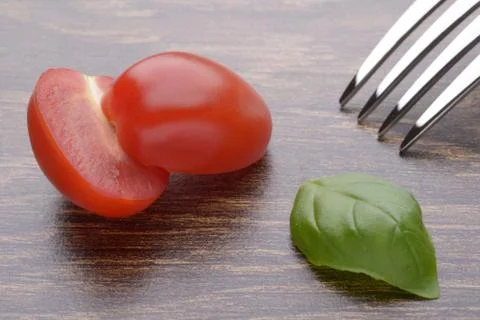 Halved cherry tomatoes and basil leaves on a dark table. Fork. Stock Photos