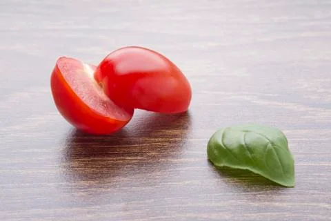 Halved cherry tomatoes and basil leaves on a dark table. Stock Photos