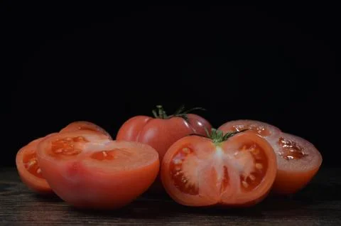 Halved tomato on a dark table with a falling salt on a black background. Stock Photos