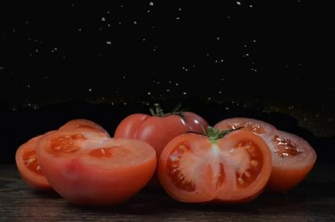 Halved tomato on a dark table with a falling salt on a black background. Stock Photos