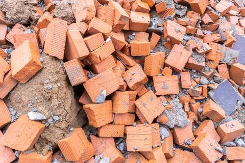 Halves of bricks lie randomly on clay soil, construction waste is piled up in Stock Photos