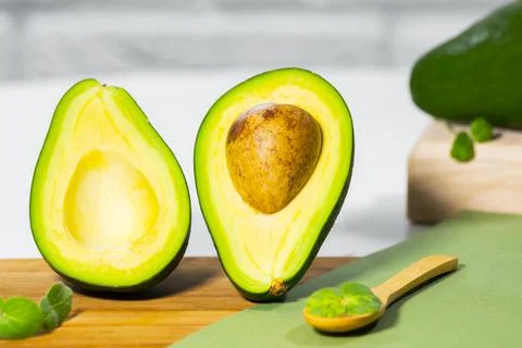 Halves of Ripe Avocado and micro green on wooden board served on table, white Stock Photos