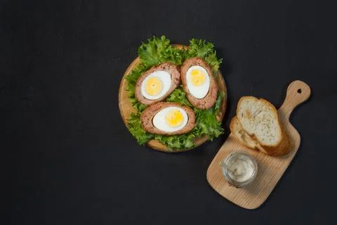 Halves of a Scotch egg on a wooden stand with lettuce leaves, with toasted bread Stock Photos