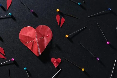 Halves of torn paper heart connected by sewing pin among other ones on blac.. Stock Photos