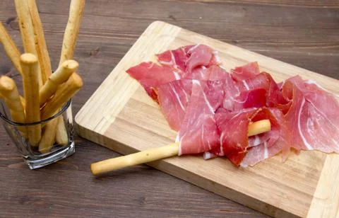 Ham on cutting board with bread sticks on wooden table Stock Photos