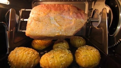 Ham or beef roast. Raw cooking meat on rotisserie with potatoes. cu Stock Footage 102139944