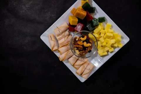 Ham rolls, diced fruit paste, cheese cubes, and nuts on square white plate Stock Photos