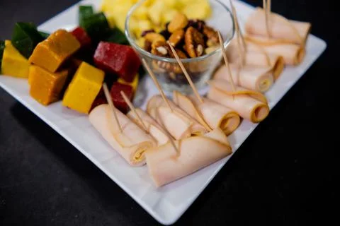 Ham rolls, diced fruit paste, cheese cubes, and nuts on square white plate Foto stock