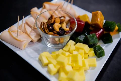 Ham rolls, diced fruit paste, cheese cubes, and nuts on square white plate Stock Photos