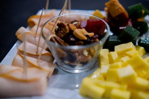 Ham rolls, diced fruit paste, cheese cubes, and nuts on square white plate Stock Photos
