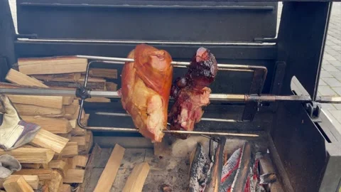 Ham rotating on spit in street grill. European street food. Big piece of pork Stock Footage 194438087