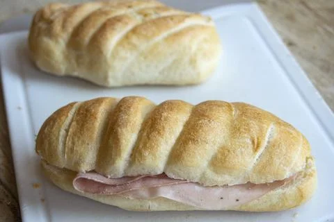 Ham sandwich roll with crusty bread on white cutting board Stock Photos