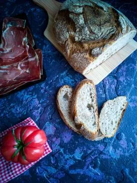Ham, tomato, bread and herbs in composition on dark background Stock Photos