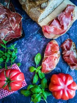 Ham, tomato, bread and herbs in composition on dark background Stock Photos