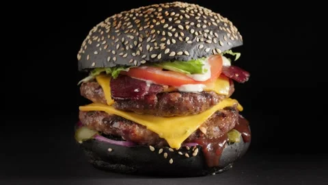 Hamburger with black bun and double beef cutlet rotates on a black background. Stock Footage 146702964
