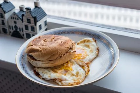 Hamburger bun scorched with fried eggs in plate Stock Photos