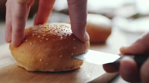 Hamburger Bun Sliced by a Sharp Kitchen Knife on a Wooden Cutting Board Vidéo 331101185